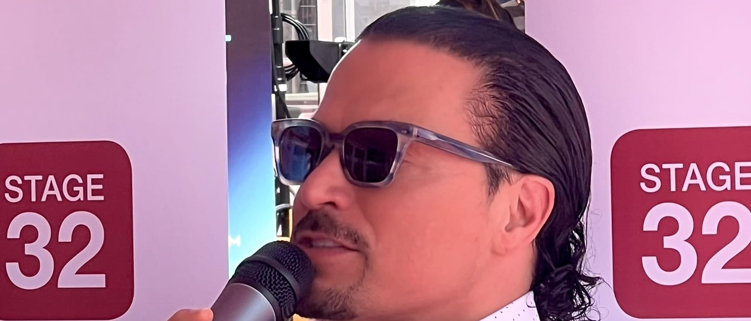 Stage 32 founder Richard Botto speaking into a microphone in front of a Stage 32 backdrop in Cannes