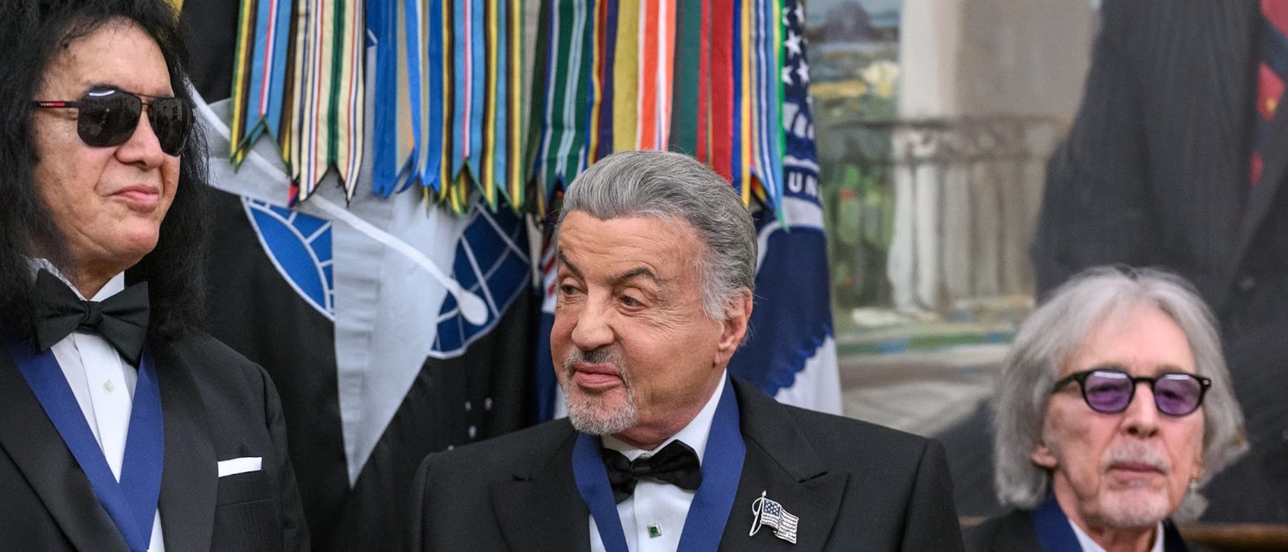 Sylvester Stallone in a tuxedo and Kennedy Center Honors medal at the White House in December 2025, between fellow honorees