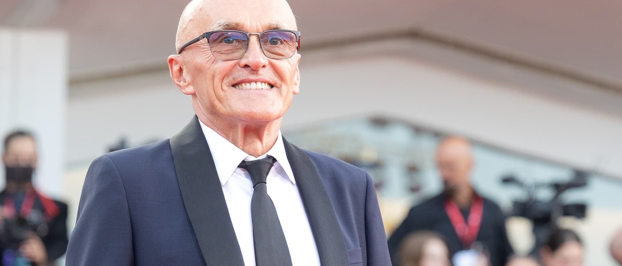 Danny Boyle, smiling, in a navy tuxedo and black tie on the red carpet at the world premiere of 'Ink' at the Venice Film Festival