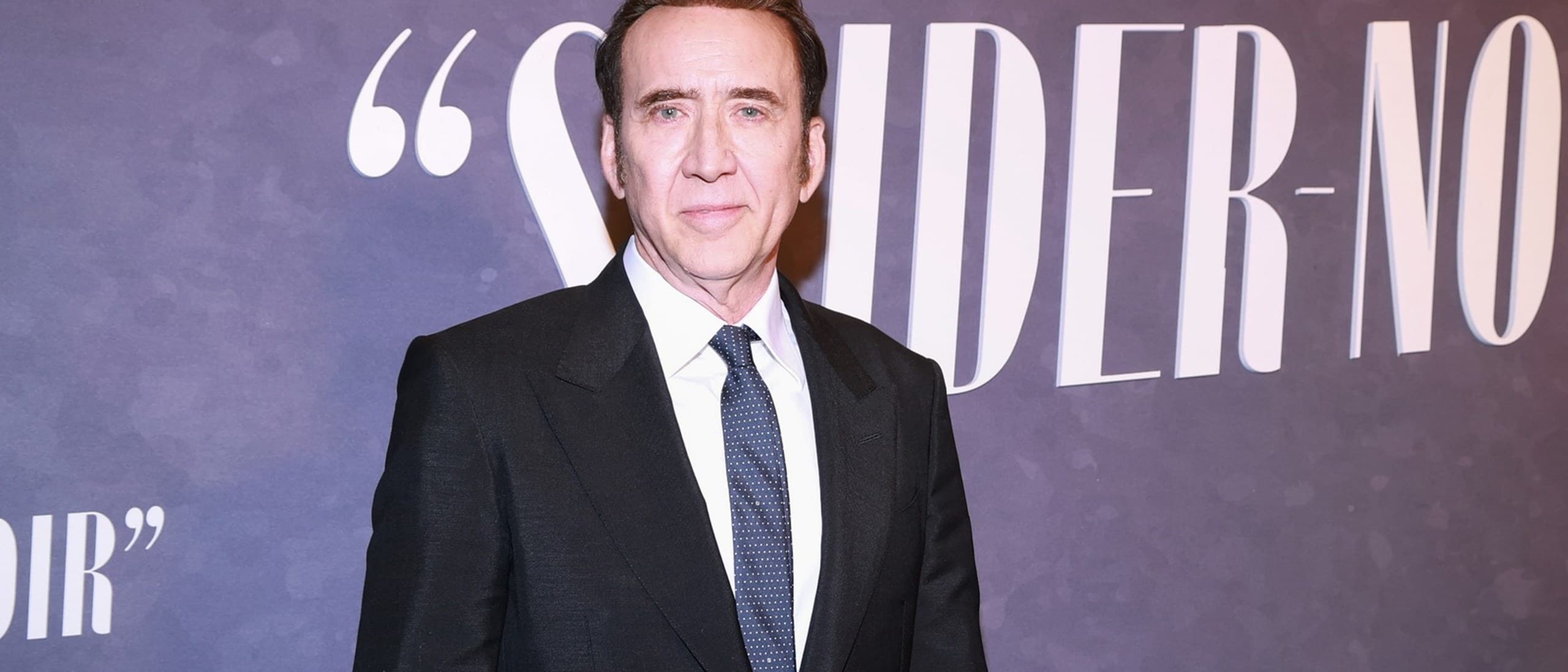 Nicolas Cage in a black suit and dotted tie in front of the Spider-Noir backdrop at the series' New York premiere