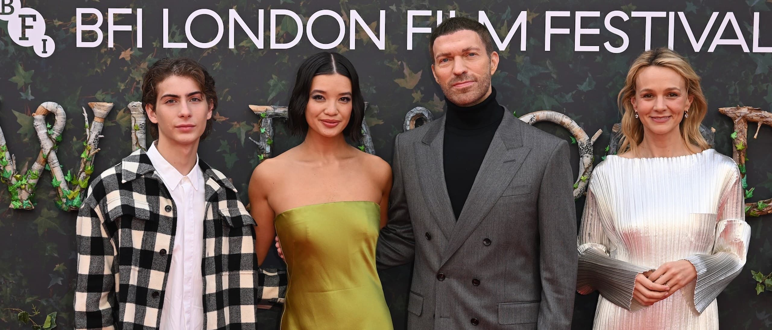 Travis Knight in a grey suit and black turtleneck on the red carpet at the BFI London Film Festival world premiere of Wildwood, standing with voice cast members Jacob Tremblay, Peyton Elizabeth Lee and Carey Mulligan in front of an ivy-covered Wildwood backdrop