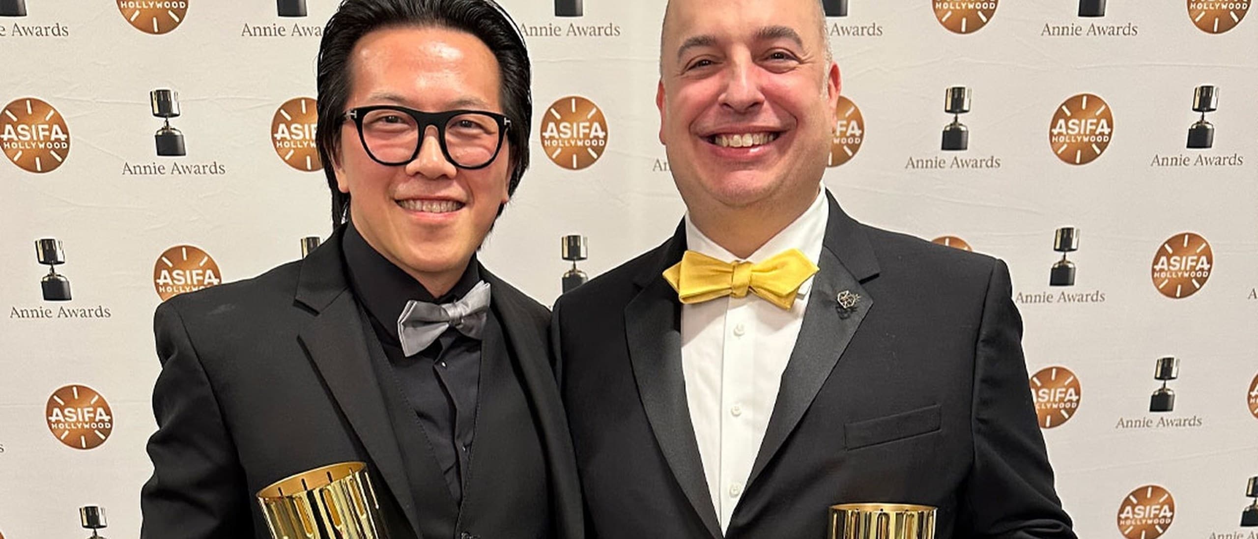 LightBox Expo co-founders Bobby Chiu, left, and Jim Demonakos in black tie holding their Annie Awards in front of the ASIFA-Hollywood press wall