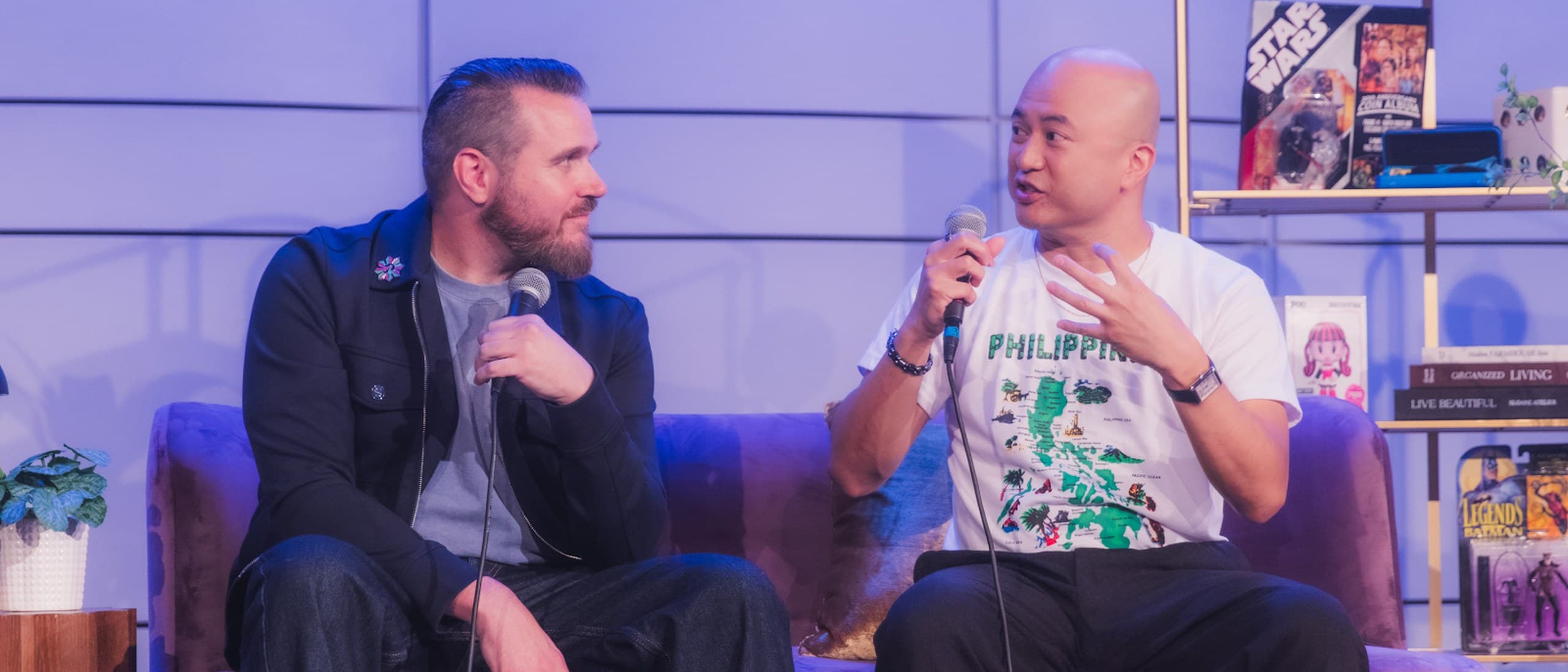 Directors Joel Crawford and Januel Mercado sitting on a purple sofa on stage at MultiCon 2026, Mercado speaking into a microphone while Crawford listens
