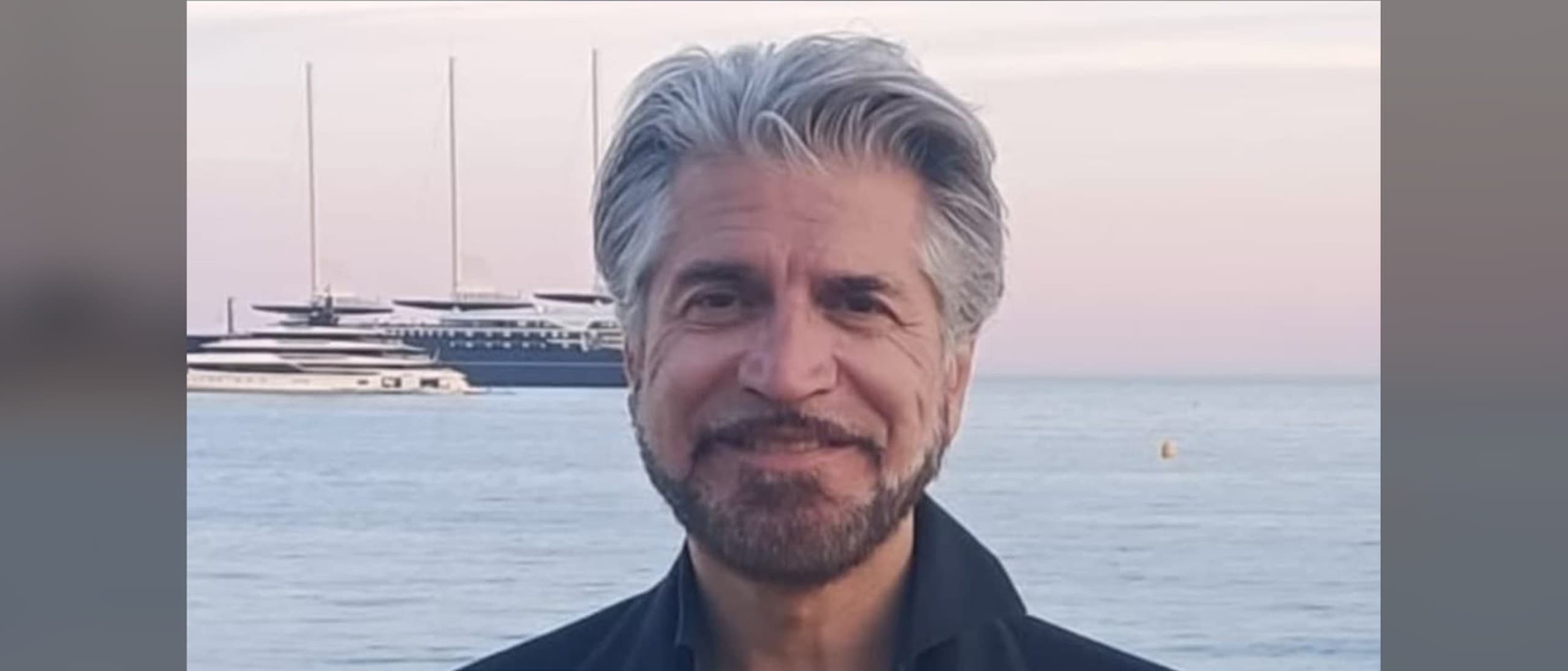 Jean Mach, co-founder of the French AI studio Inevitable, smiling on the Cannes seafront at dusk with yachts behind him